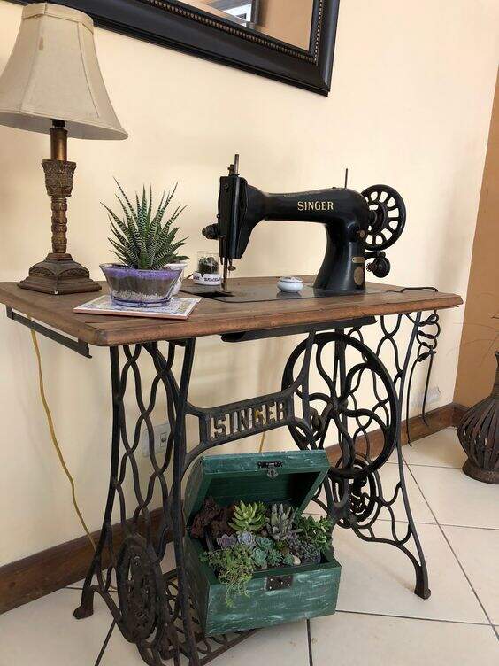 máquina de costura com a mesa, como aparador, com abajur e algumas plantas.