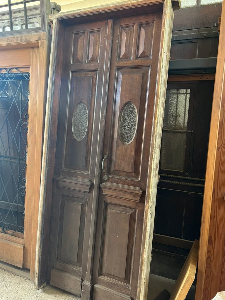 Porta de madeira cor escura, com almofadas e vidro ao centro.
