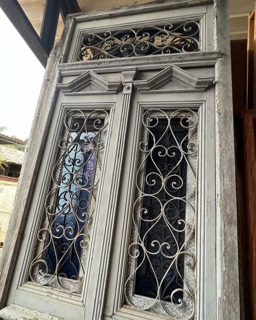Porta antiga com diversos detalhes encantadores. Grades de ferro, postigos e bandeira superior.