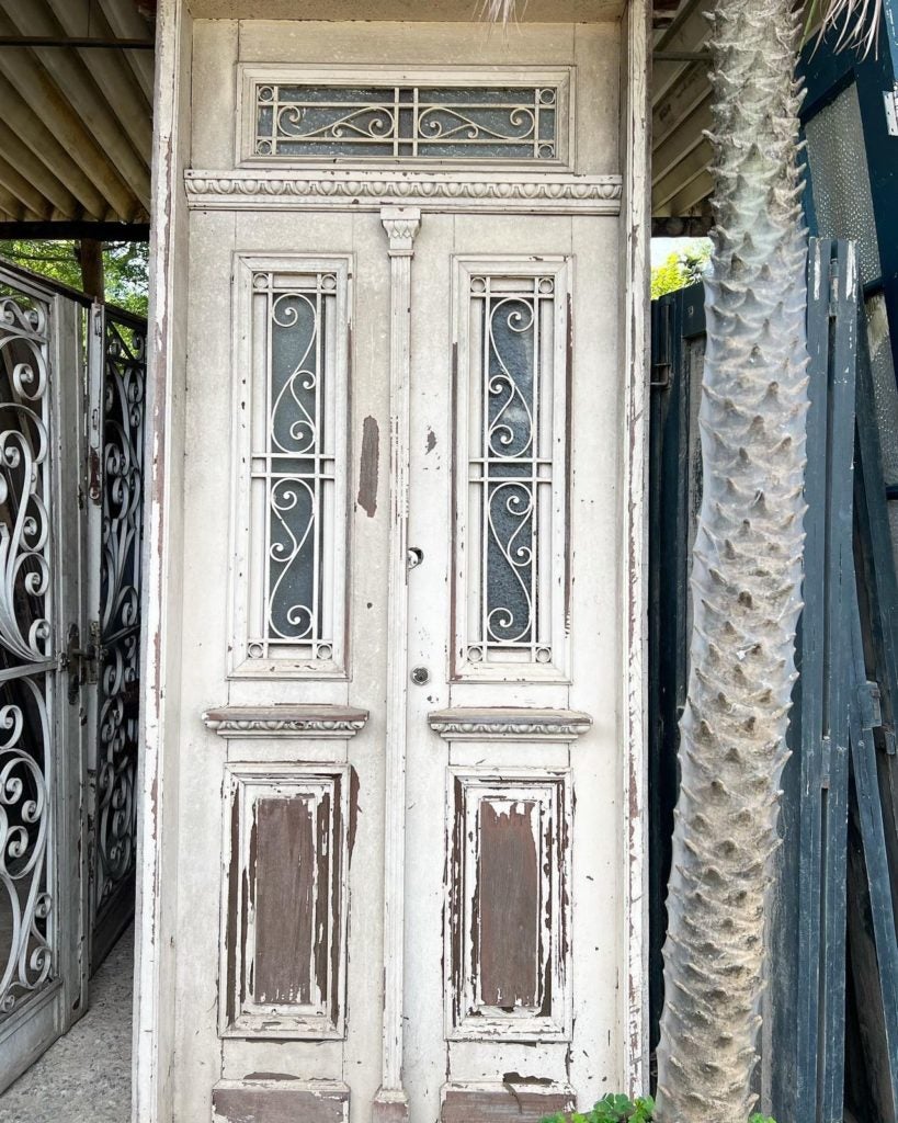 Porta dupla antiga, de demolição, com grade e postigo, possui bandeira superior com grade e vidro.