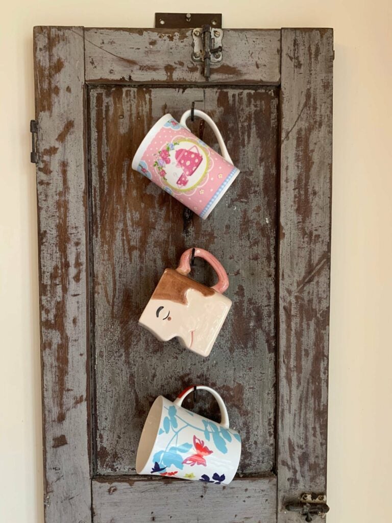 Porta xícaras feito a partir de folha de madeira de janela antiga, peça de reuso ideal para decoração funcional. Disponível no site e na loja física.