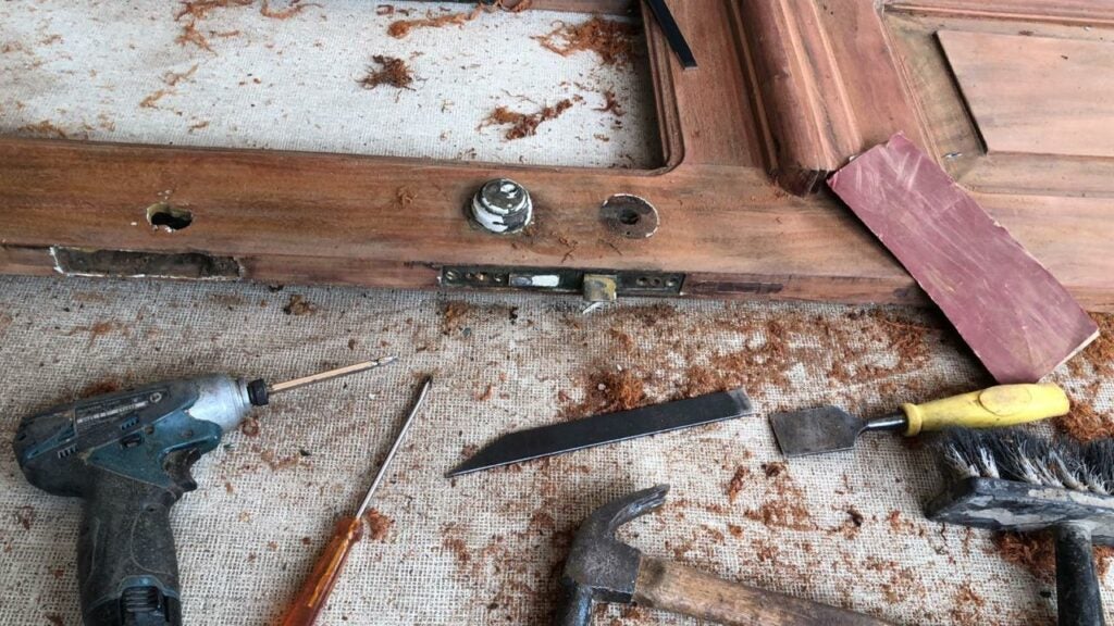 Ferramentas de marcenaria sobre bancada durante processo de restauração de peça de madeira antiga.