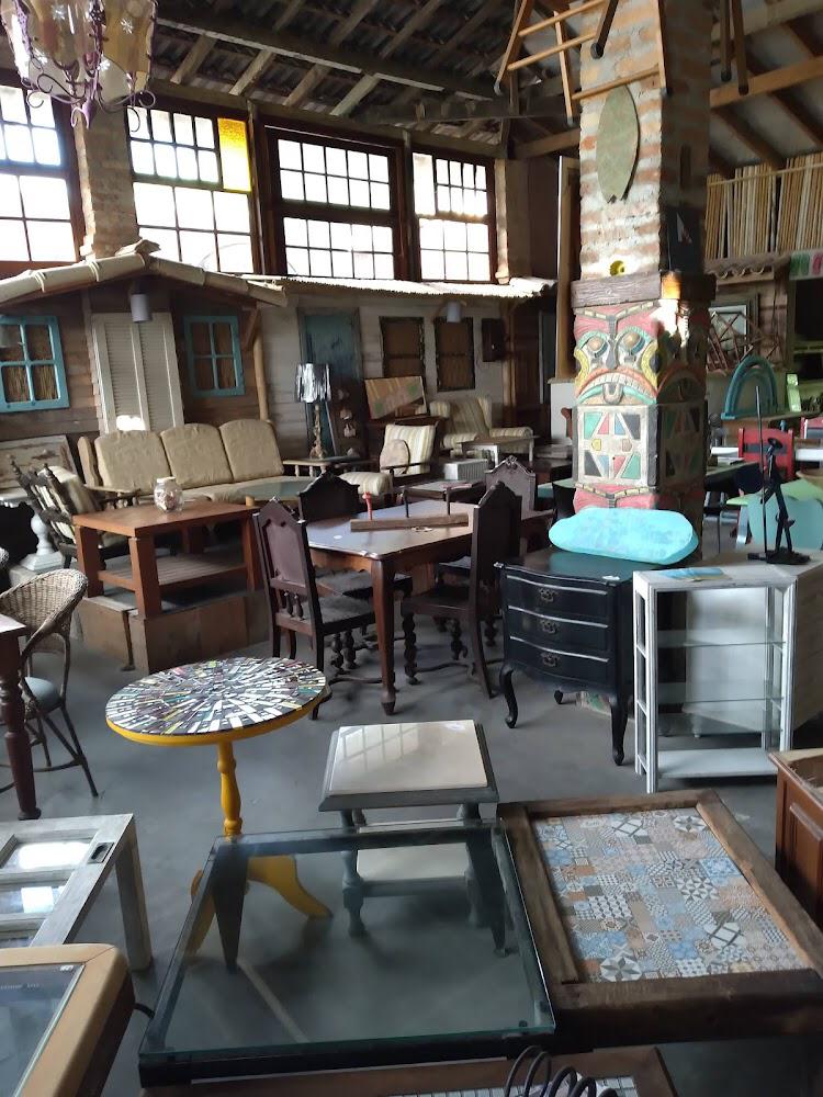 Interior de galpão com móveis antigos, peças de madeira e objetos de decoração garimpados expostos para reutilização e restauração.